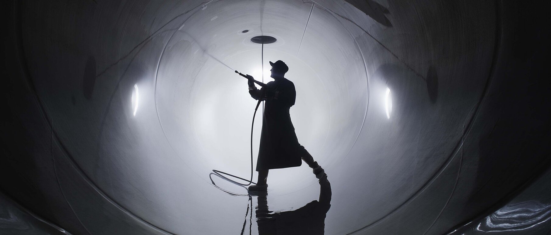 Man in safety clothing stands in a pipe and cleans it with a high-pressure cleaner